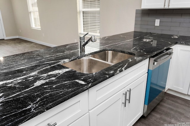 kitchen featuring stainless steel dishwasher, white cabinets, sink, and dark stone counters