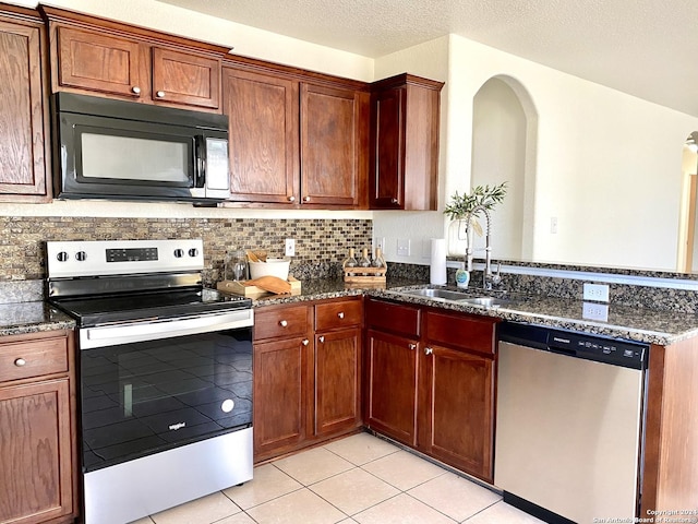 kitchen with a textured ceiling, stainless steel appliances, sink, light tile patterned floors, and dark stone countertops