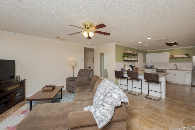 living room featuring a textured ceiling, ceiling fan, crown molding, and sink