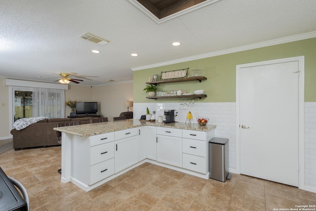 kitchen featuring kitchen peninsula, light stone countertops, white cabinets, and ornamental molding