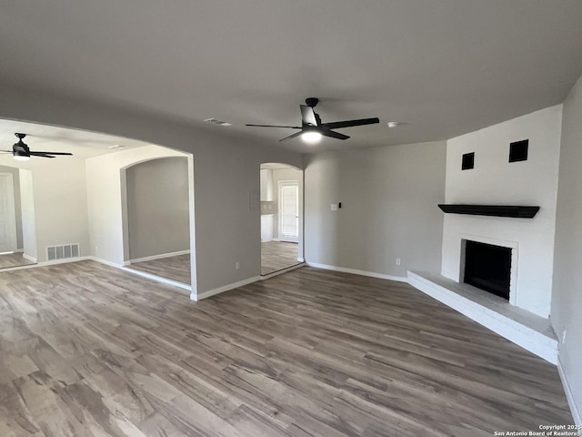 unfurnished living room with ceiling fan, a fireplace, and wood-type flooring