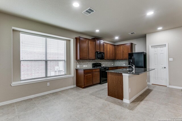 kitchen with backsplash, an island with sink, dark stone countertops, and black appliances