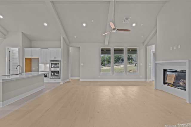 unfurnished living room with sink, high vaulted ceiling, light hardwood / wood-style flooring, beamed ceiling, and ceiling fan