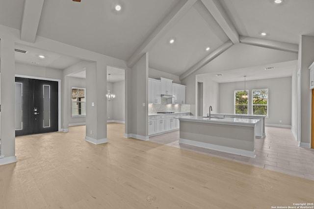 kitchen with sink, white cabinetry, a notable chandelier, an island with sink, and light wood-type flooring