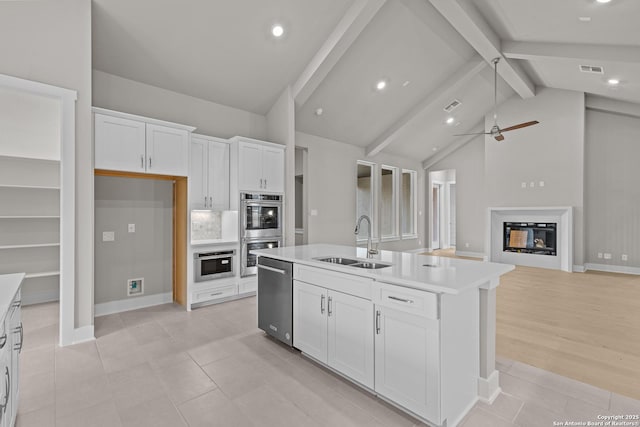 kitchen with white cabinetry, sink, vaulted ceiling with beams, a kitchen island with sink, and stainless steel appliances