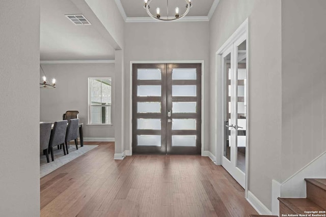 entrance foyer with an inviting chandelier, wood-type flooring, crown molding, and french doors