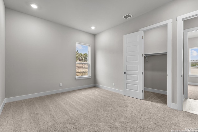 unfurnished bedroom featuring multiple windows, a walk in closet, light colored carpet, and a closet