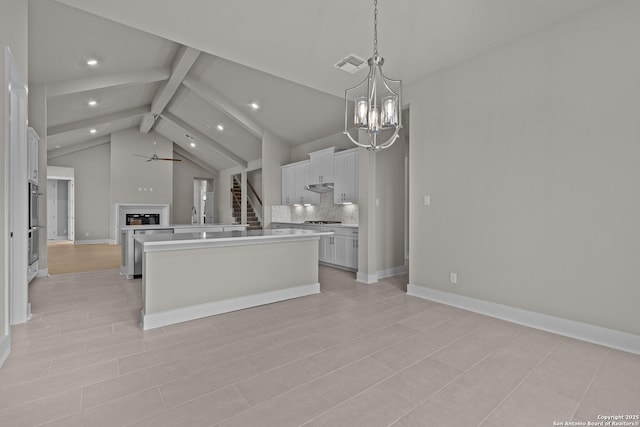 kitchen with a kitchen island, pendant lighting, beamed ceiling, white cabinetry, and backsplash