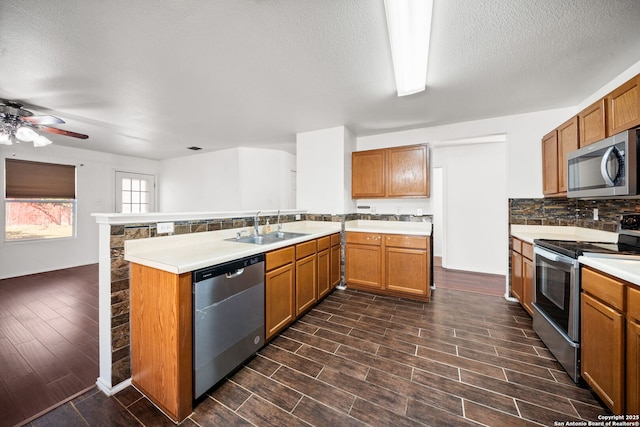 kitchen featuring sink, decorative backsplash, a textured ceiling, appliances with stainless steel finishes, and kitchen peninsula