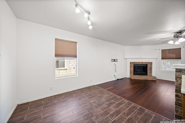 unfurnished living room featuring a textured ceiling, a brick fireplace, plenty of natural light, and ceiling fan