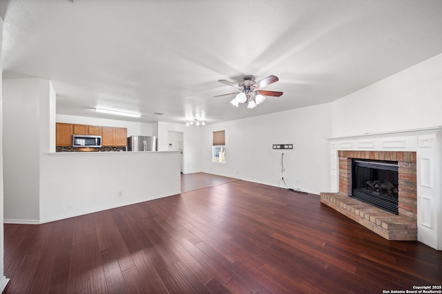 unfurnished living room with dark hardwood / wood-style flooring, a brick fireplace, and ceiling fan