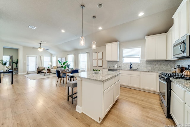 kitchen with a center island, lofted ceiling, ceiling fan, appliances with stainless steel finishes, and white cabinetry