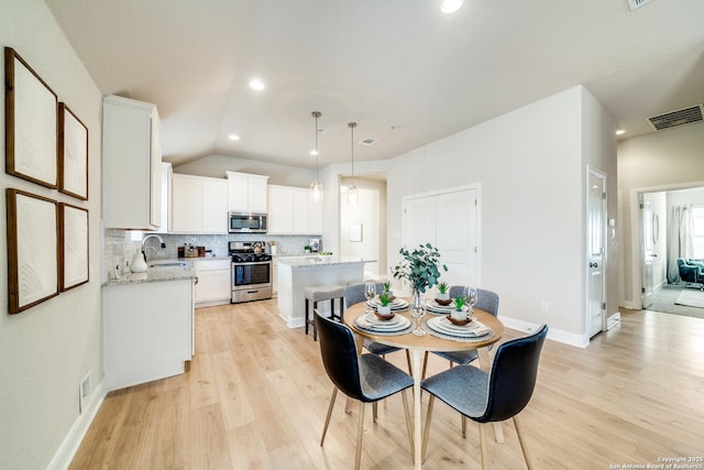 dining area with light wood-type flooring, lofted ceiling, and sink