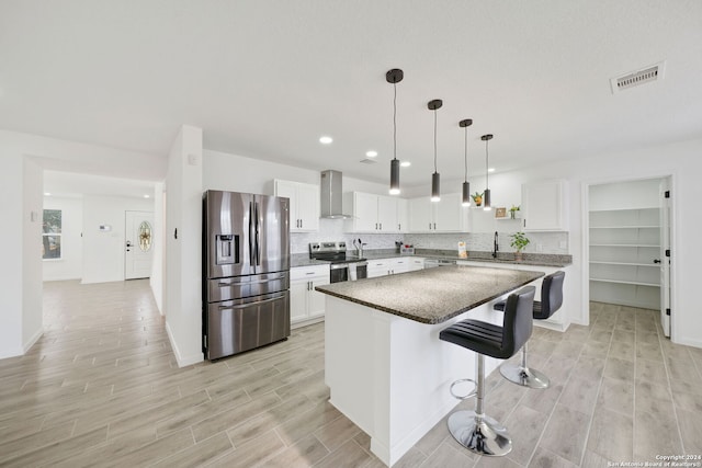 kitchen with wall chimney range hood, a kitchen island, white cabinets, stainless steel appliances, and a breakfast bar area