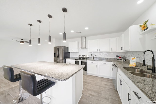 kitchen featuring white cabinets, decorative light fixtures, sink, stainless steel appliances, and wall chimney exhaust hood