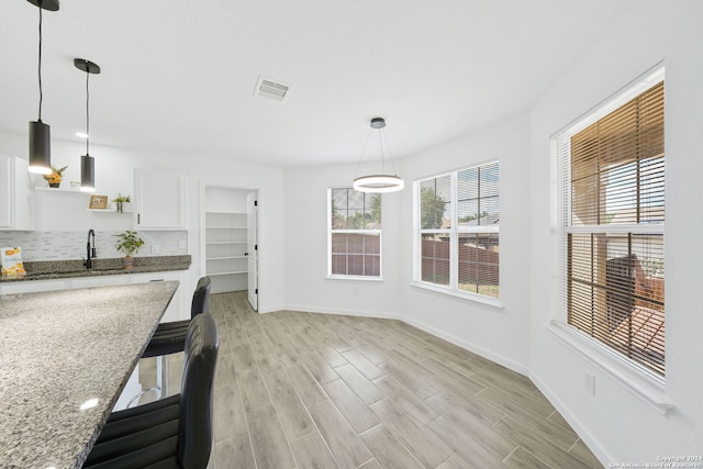 kitchen featuring light hardwood / wood-style floors, light stone countertops, white cabinetry, decorative light fixtures, and backsplash