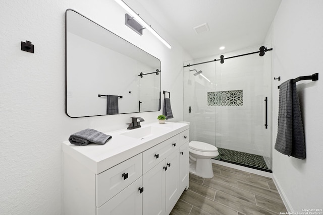 bathroom featuring a shower with shower door, toilet, and vanity