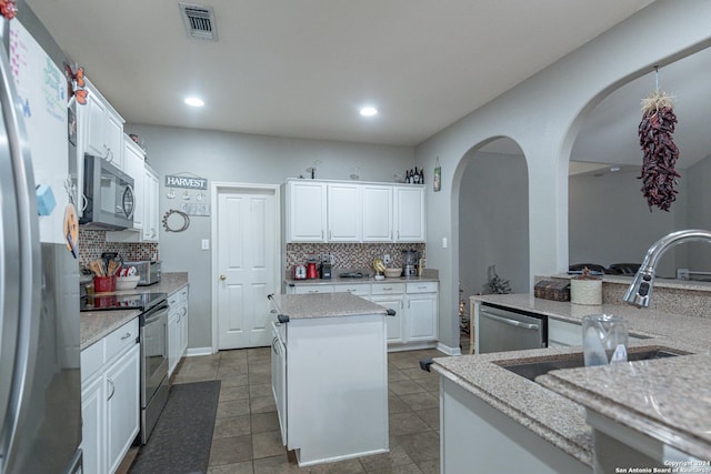 kitchen featuring backsplash, a kitchen island, light stone counters, white cabinetry, and stainless steel appliances