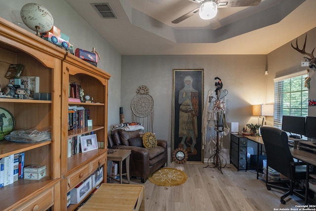 home office featuring light wood-type flooring, a raised ceiling, and ceiling fan