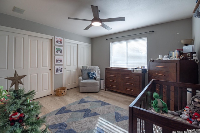 bedroom with ceiling fan, light hardwood / wood-style flooring, and two closets