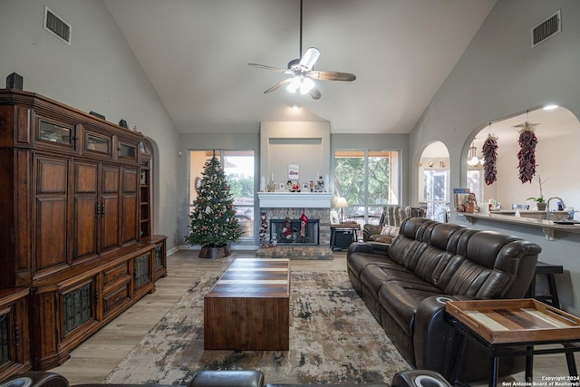 living room featuring a stone fireplace, ceiling fan, light hardwood / wood-style flooring, and plenty of natural light