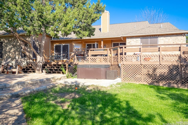 rear view of property featuring a hot tub, a deck, and a lawn