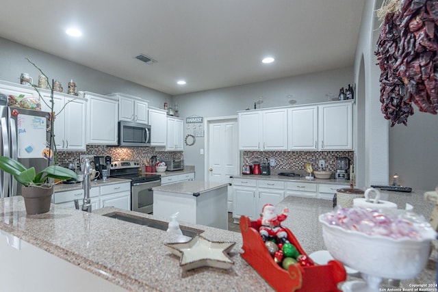 kitchen featuring kitchen peninsula, light stone counters, white cabinetry, and stainless steel appliances