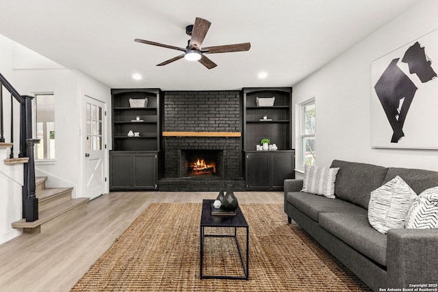 living room featuring hardwood / wood-style flooring, ceiling fan, built in features, and a brick fireplace