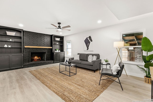 living room featuring a fireplace, built in shelves, light hardwood / wood-style flooring, and ceiling fan