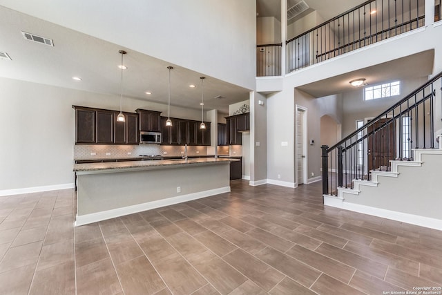 kitchen featuring light stone countertops, decorative backsplash, dark brown cabinets, a high ceiling, and hanging light fixtures