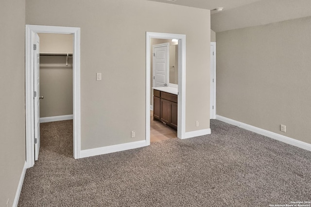 unfurnished bedroom featuring light carpet, a walk in closet, ensuite bath, and a closet