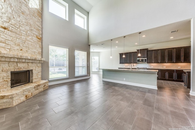 kitchen featuring decorative backsplash, a towering ceiling, pendant lighting, a stone fireplace, and an island with sink