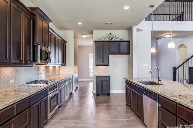 kitchen featuring sink, stainless steel appliances, light stone counters, decorative light fixtures, and dark brown cabinets