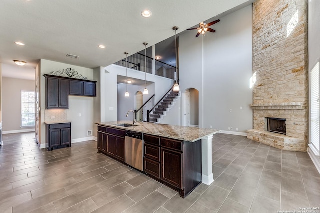 kitchen featuring sink, hanging light fixtures, stainless steel dishwasher, a fireplace, and light stone counters