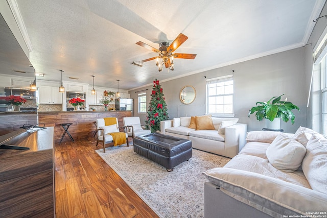 living room featuring hardwood / wood-style flooring, ceiling fan, crown molding, and a textured ceiling