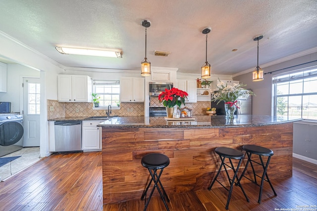 kitchen with white cabinets, dark stone countertops, appliances with stainless steel finishes, a breakfast bar area, and washer / clothes dryer