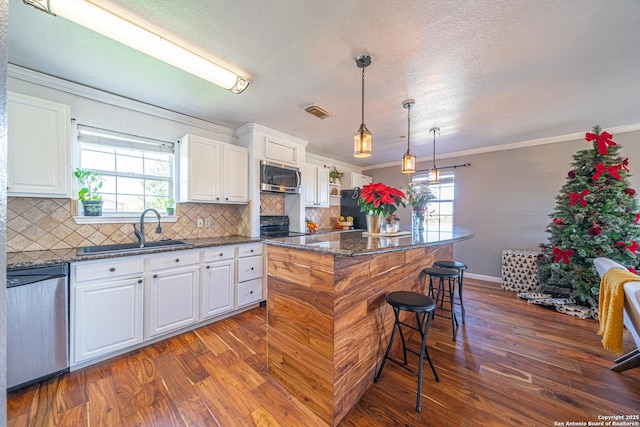 kitchen featuring sink, dark stone countertops, appliances with stainless steel finishes, a kitchen island, and white cabinetry