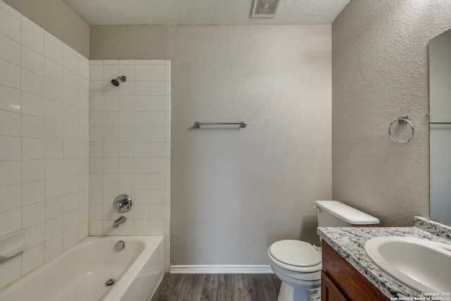 full bathroom with wood-type flooring, a textured ceiling, toilet, vanity, and tiled shower / bath