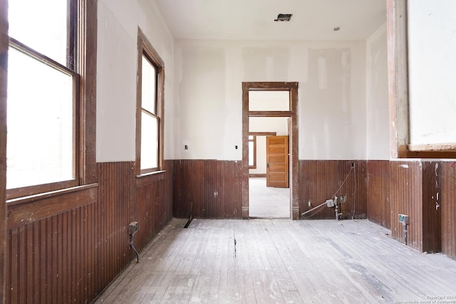 empty room with a wealth of natural light, light hardwood / wood-style flooring, and wood walls