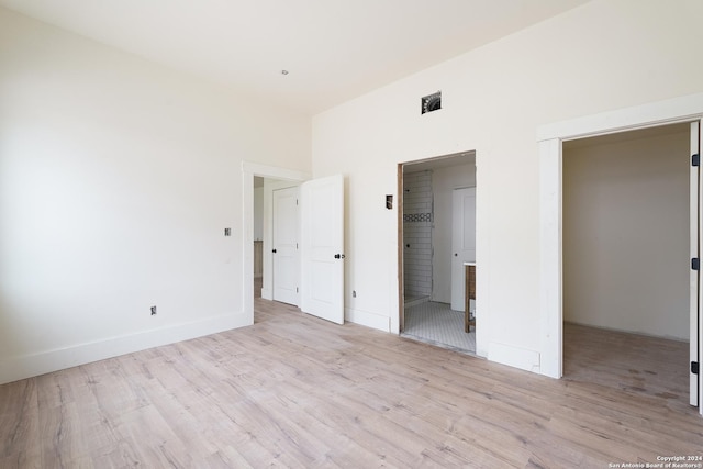 unfurnished bedroom with ensuite bathroom and light wood-type flooring