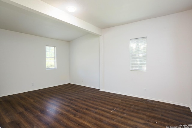 empty room with beamed ceiling and dark wood-type flooring