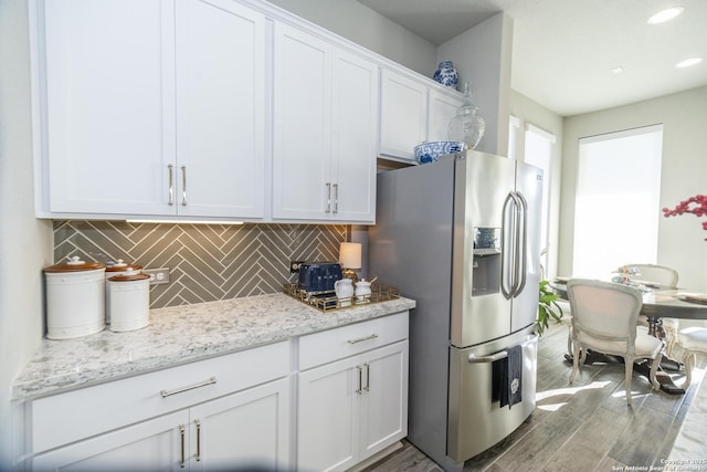 kitchen with white cabinetry, light stone counters, light hardwood / wood-style flooring, backsplash, and stainless steel fridge