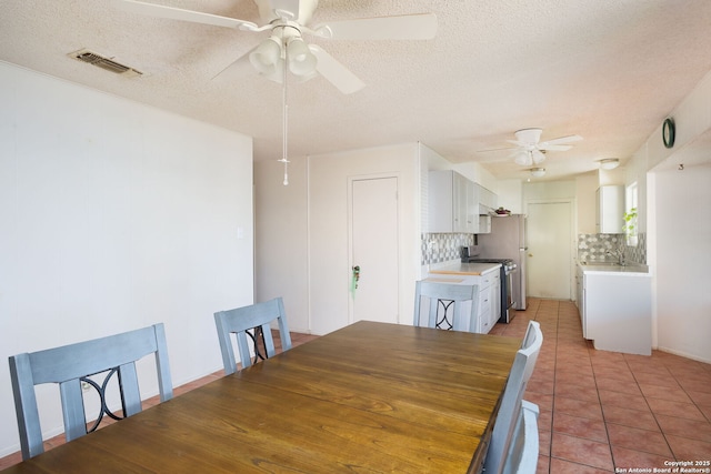 unfurnished dining area featuring ceiling fan, sink, light tile patterned floors, and a textured ceiling