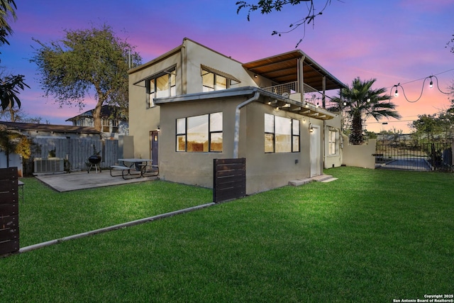 back house at dusk with a balcony, central AC, and a lawn