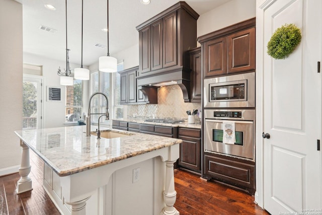 kitchen with dark brown cabinetry, sink, dark hardwood / wood-style flooring, pendant lighting, and a kitchen island with sink