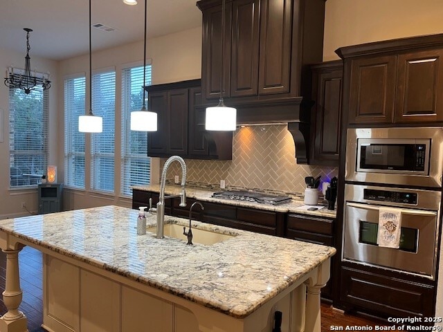 kitchen featuring pendant lighting, light stone countertops, an island with sink, and appliances with stainless steel finishes