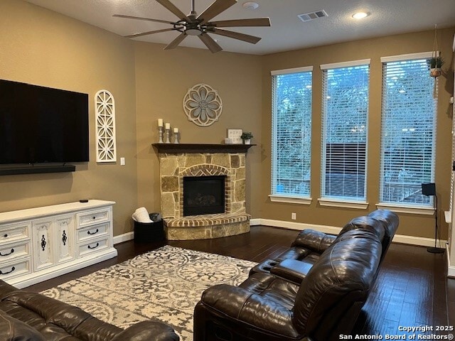 living room with ceiling fan, dark hardwood / wood-style flooring, and a stone fireplace