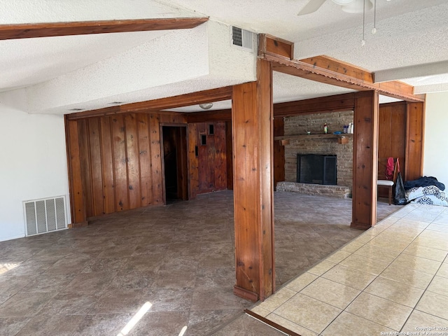 unfurnished living room featuring a fireplace, ceiling fan, a textured ceiling, and wooden walls