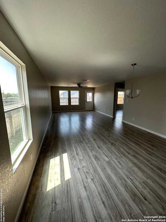 unfurnished living room featuring ceiling fan with notable chandelier, dark hardwood / wood-style flooring, and a textured ceiling