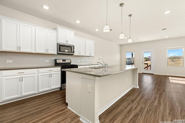 kitchen with a center island with sink, white cabinets, sink, appliances with stainless steel finishes, and decorative light fixtures